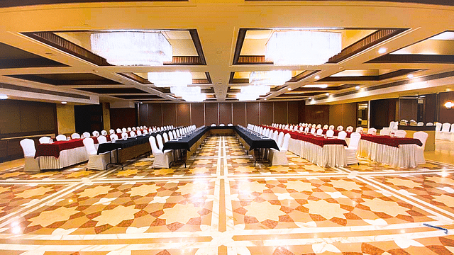 A spacious banquet hall at Pride Plaza Ahmedabad, featuring multiple rows of tables with red tablecloths, set up for a large conference or event.